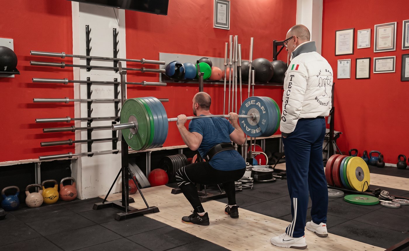 Il coach assiste un atleta durante uno squat pesante