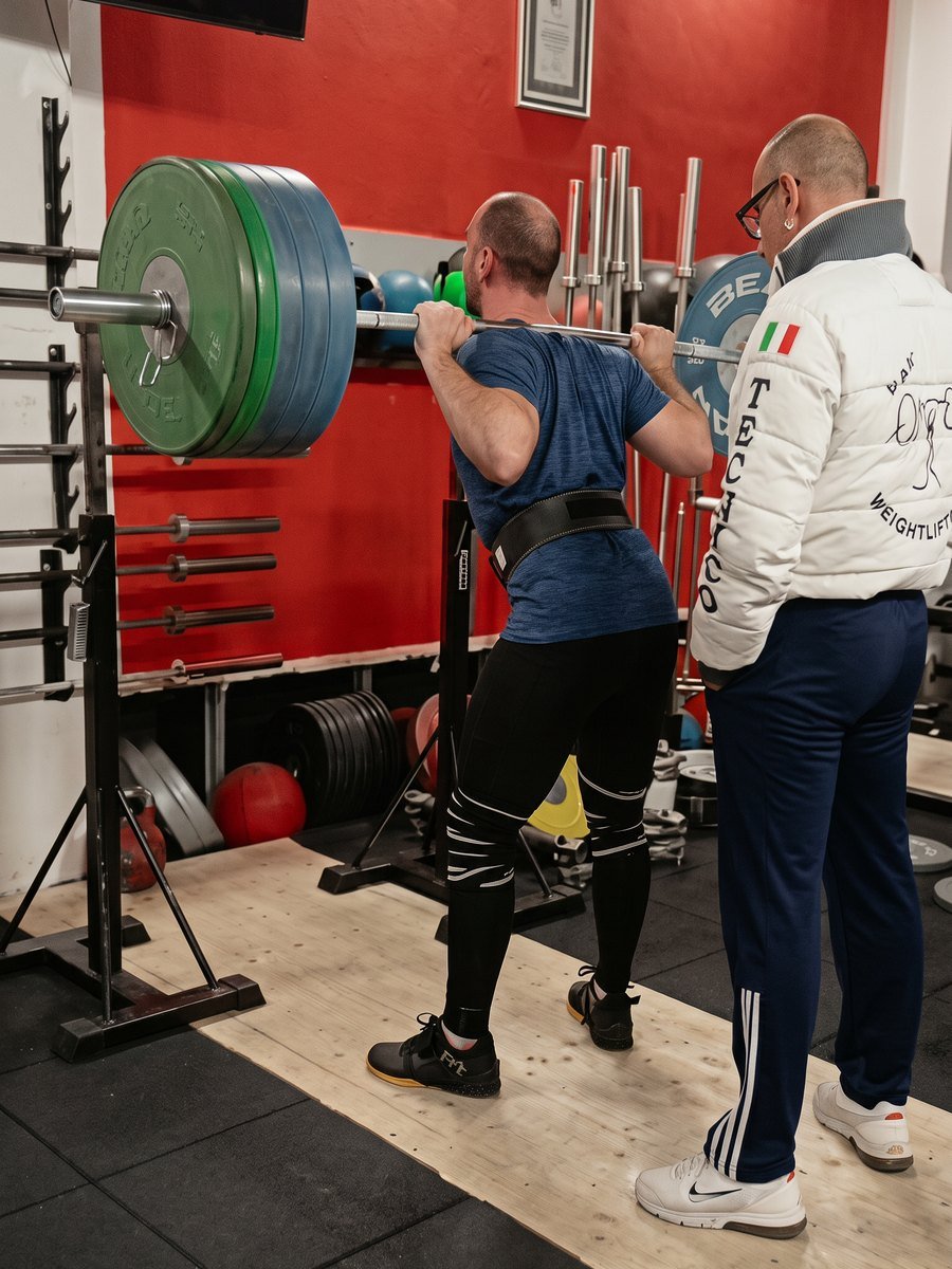 Il coach della Mak Training assiste un atleta durante uno squat pesante